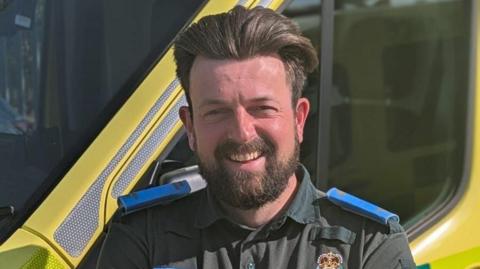 Luke Rapela - a young man with brown hair combed back and a short beard 