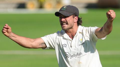 Kiran Carlson wearing a cap with clenched fists and and arms out wide in celebration