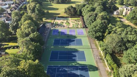 A drone view of Bury Knowle Park on a sunny day. The tennis court is visible, as well as the mini gold area.