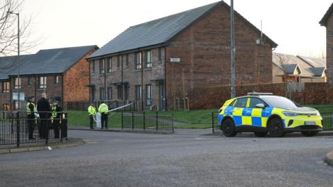 A police car and five uniformed officers outside some modern brown brick houses in Paisley