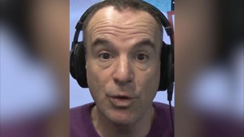 A man, Martin Lewis wears a purple jumper and headphones and looks at the camera