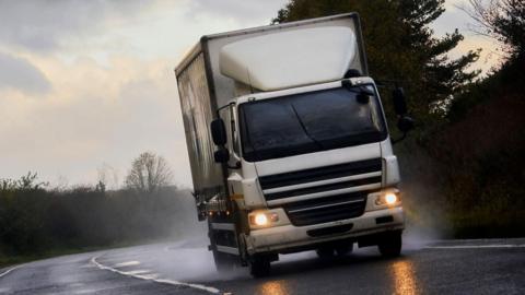 A white lorry driving on a wet road
