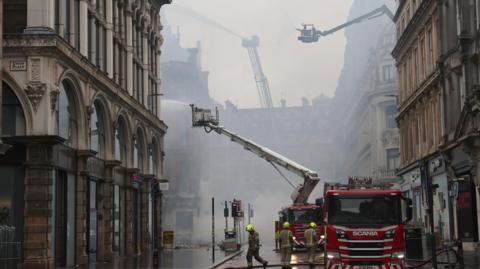 Fire crews and appliances in the centre of Glasgow. There is a lot of smoke and aerial applinces are spraying water on the building.