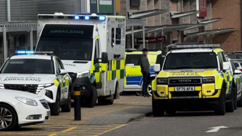 Police Scotland and Scottish Ambulance Service parked next to a row of shops at Inverness' Inshes Retail Park.