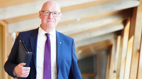 John Swinney walks in the parliament ahead of the debate