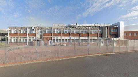 An outside shot of the brown brick factory building which has lots of windows.