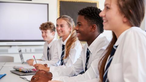 Four GCSE students in uniform in a classroom smile as they discuss an English Language topic.