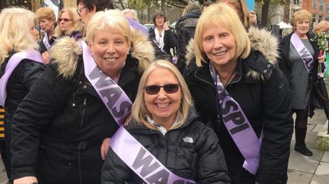 Sisters (left to right) Mary Waterhouse, Norma Elkington and Susan Dutton wearing black coats and lilac sashes with 'Waspi' written on them at a campaign rally