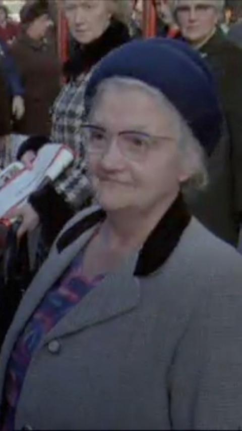 An older woman wearing a wooly hat and glasses smiles at an interview