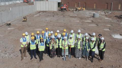 A group of people wearing hi-vis vests and helmets on the site, which is being prepared for building work.