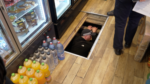 A police officer emerges from beneath the floorboards of a shop.