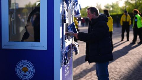 A Leicester fan purchases a matchday programme
