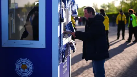 A Leicester fan purchases a matchday programme