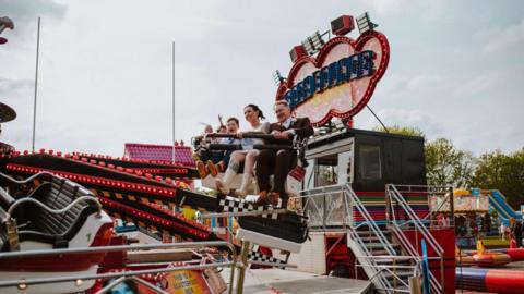A couple who have just got married sitting on a fairground ride with their son 