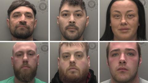 A composite image showing police custody photos of six people arranged in two rows of three. The pictures show head and shoulder images against grey backgrounds. Top row, from left: A man with black hair and beard; a man with short curly brown hair and beard; a woman with long black hair. Bottom row, from left: A man with a shaved head and full brown beard wearing a green T-shirt; a man with short fair hair and full beard wearing a black top; a man with short fair hair and closely cropped beard wearing a light-grey T-shirt. 