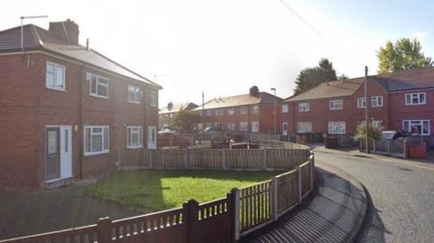 A street with houses lined on either side, there is a bend in the road and the houses are red brick semi-detached