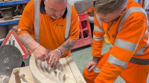 Dave Hindmarch and Josh Widdowson work on a piece of stone, wearing bright orange uniforms.