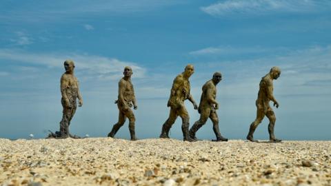 Five statues of men in different poses as if walking