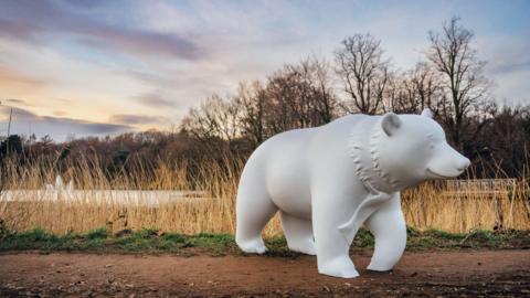 A white sculpture of a bear in a park by a lake in Leeds as part of a charity bear hunt trail 