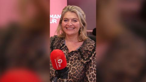 Bryony Gordon wearing a leopard print shirt with a large collar. She's smiling and sat in front of a red mic.