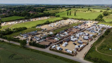 An aerial view of lots of caravans and static homes on brownfield land, surrounded by green fields.