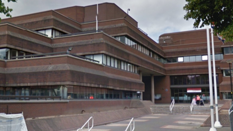 A brown building of at least three storeys. More than half a dozen steps, with two white hand rails on them, are near the building in the background.