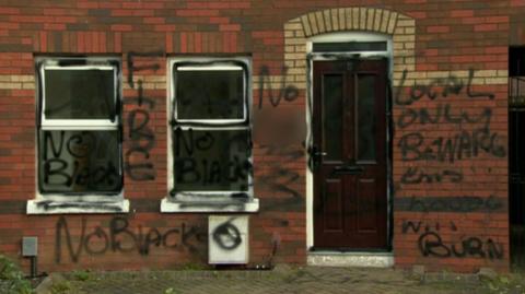 The front of a house covered in graffiti. The graffiti reads "No blacks", "Fire", and "Local only beware this house will burn".