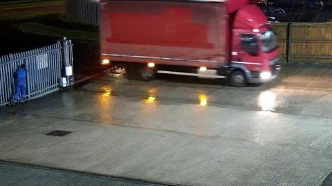 A still image provided by Blancomet shows a red HGV driving onto the firm's concrete forecourt through metal security gates. A man in a blue outfit stands next to the gates. Text on the CCTV image give the date as 18/01/2026, a time of 22:15:01 and says Front Entrance. 