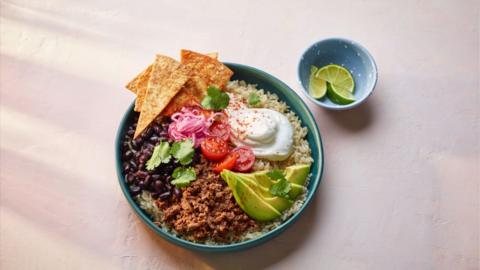 A blue bowl filled with beef, beans and rice, topped with sour cream, avocado and garnishes