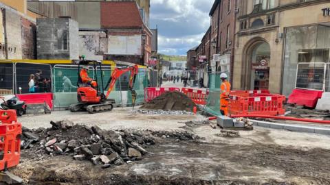 Workmen in orange uniforms dig up the pavement.