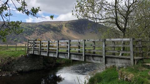 River Caldew with Carrock Fell in the background. A wooden bridge goes over the water.