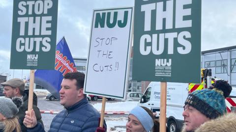Men and women on a picket line outside the STV offices in Aberdeen, holding placards which say Stop the Cuts.
