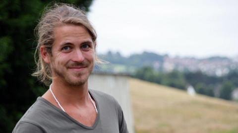 A photo of James Strawbridge. He is wearing a grey top and the background is blurred.