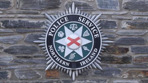 A PSNI badge on a grey brick wall.