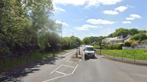 A Google street view screenshot of the A694 Lockhaugh Road, Rowlands Gill, Gateshead. There are trees either side of the road and the sky is blue and cloudy. 