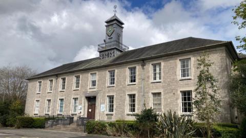 County Hall at Kendal. It is a grand two-storey stone building with a clock tower. A handful of steps lead to the entrance.