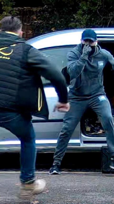 A man confronts another man in a cap and a face covering