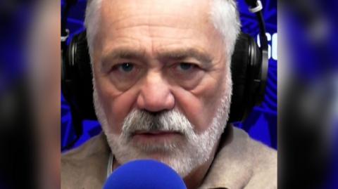 David Wilson - man with white hair and white beard, wearing headphones and speaking into a blue microphone