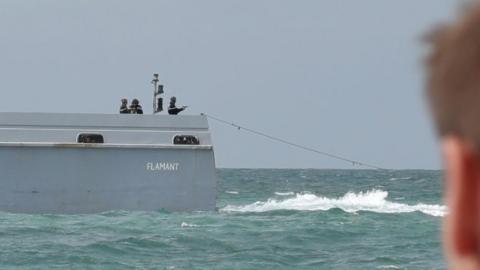 A French patrol officer at the back of the boat pointing a pistol towards the sea