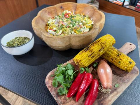 Large bowl of BBQ corn salad and two corn on the cobs on a side platter, with some red chilli and onions.