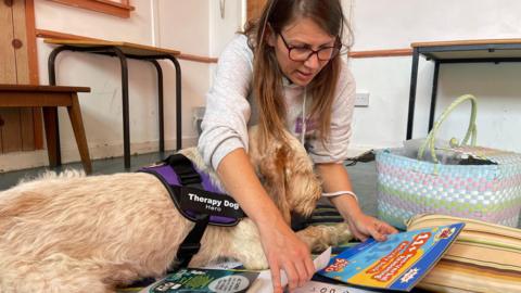 Hero the therapy dog is sat on the floor with her trainer Vicky Skinner who is preparing for a session with a student