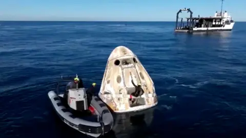 Safety team checks on dragon capsule as it bobs in ocean
