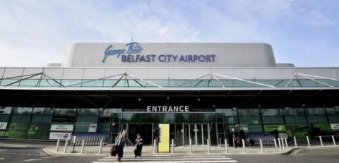 Front entrance of George Best Belfast City Airport showing two people with hand luggage walking out