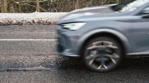 A car driving across the road with snow at the sides of the road