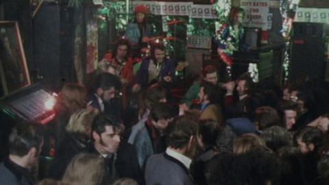 A crowd of people dance at a rock and roll pub. A band plays in the background