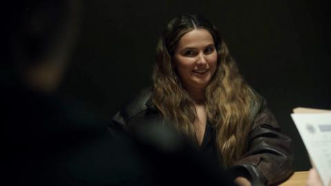 Young woman gives knowing smile to the side in a darkly lit room