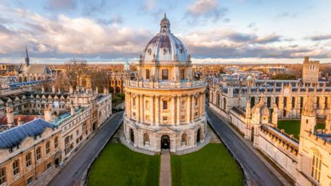 An aerial view of the Radcliffe Camera in Oxford a palladian style building which serves as a reading room for the Bodleian Library, to the south of the Old Bodleian, north of St. Mary's Church and between Brasenose College (west) and All Souls College (east) which can be seen surrounding the building.