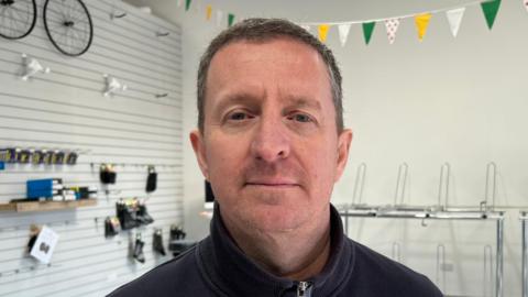 Mark Reynolds standing in his shop with empty shelves behind him