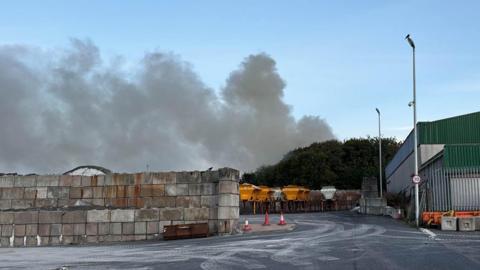 clouds of smoke above trees behind an empty car park