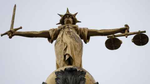 A close up of a statue on a court building. It is of a figure holding a set of scales in one out-stretched hand and a sword in the other.